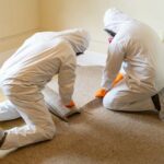 Technicians in protective gear removing water-damaged carpet during flood repair