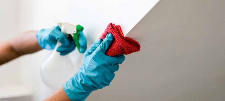 Flood Repair Tips - Close-up of hands cleaning and disinfecting water-damaged walls with gloves and disinfectant spray.